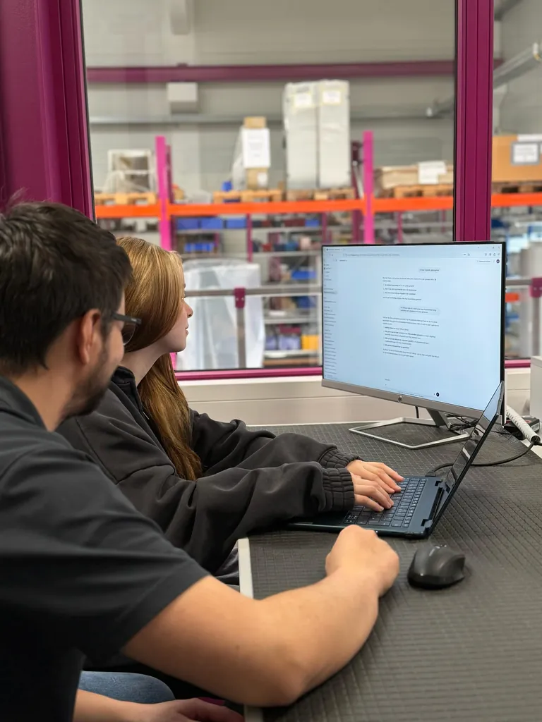 Ausbilder Martin Bielmeier und Auszubildende Corina Hinterberger arbeiten an einem Computer mithilfe eines Chatbots.