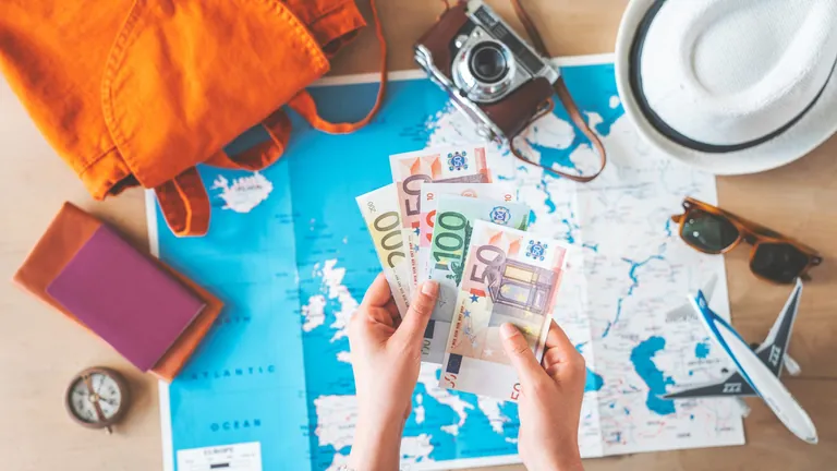 Hand mit Geld und Urlaubsutensilien