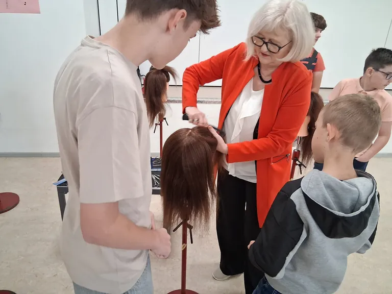 Eine Fris&ouml;rin trennt eine Partie Haare an einem k&uuml;nstlichen Frisierkopf ab.