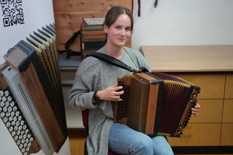 Junge Frau mit Harmonika auf dem Scho&szlig; l&auml;chelt in die Kamera.