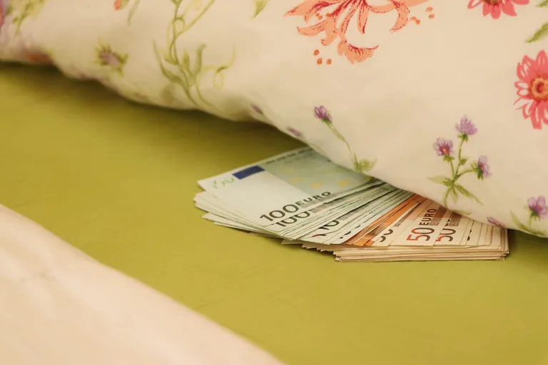 Kopfkissen mit Muster, Bündel Geld liegt darunter und schaut hervor