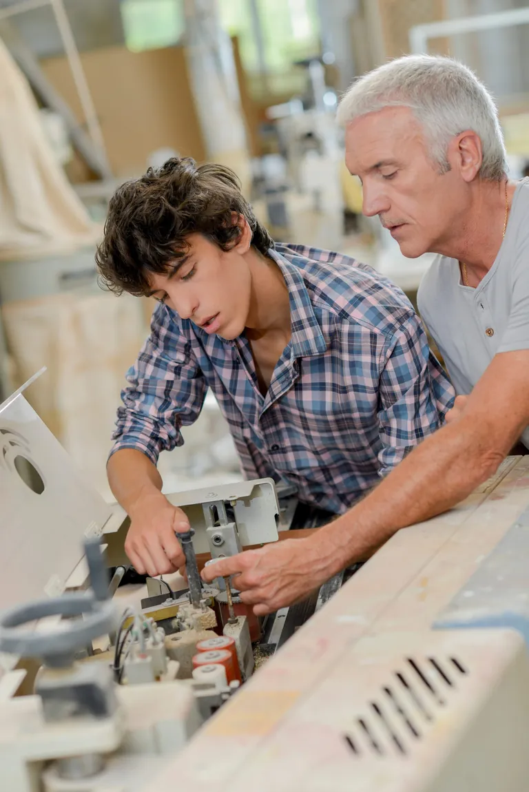 Ausbilder mit wei&szlig;en Haaren leitet Jugendlichen in Zimmerei an
