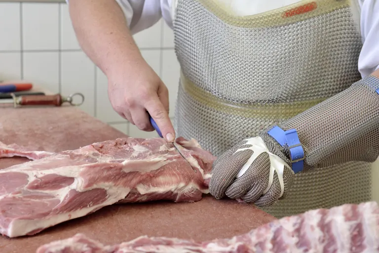 Ein Metzger schneidet Fleisch und trägt dabei einen metallenen Schutzhandschuh.