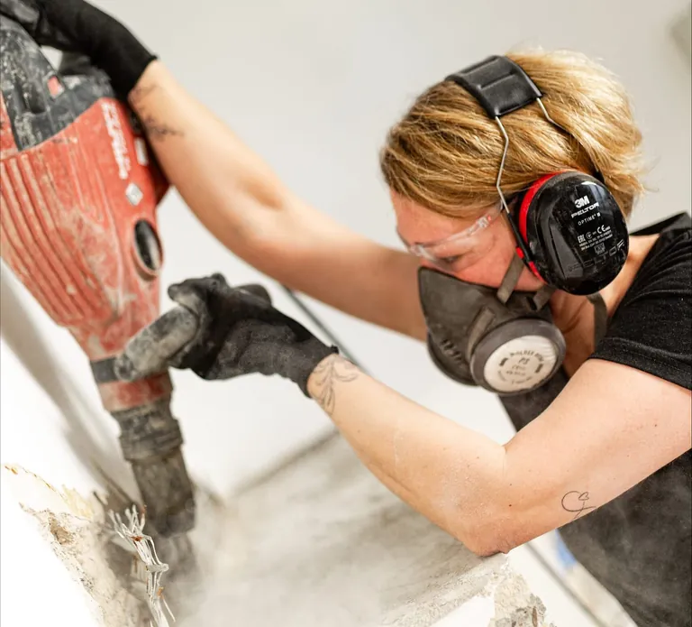 Katja Lilu Melder mit Atemschutz, Schutzbrille, Handschuhen und Geh&ouml;rschutz bei der Abbrucharbeit.
