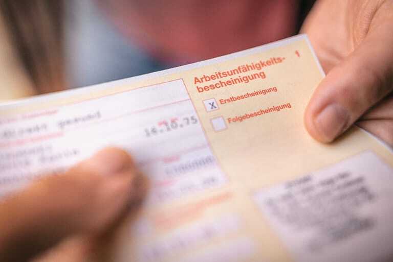 Eine Hand h&auml;lt eine Arbeitsunf&auml;higkeitsbescheinigung