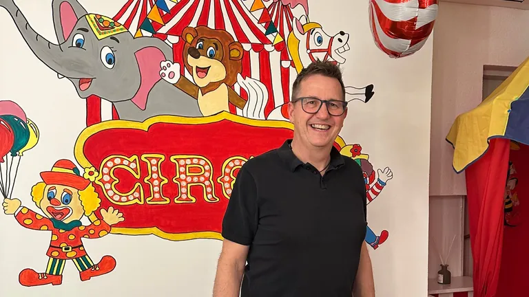 Inhaber J&uuml;rgen Meier vor der farbenfrohen Zirkus-Wandgestaltung in seinem Salon.