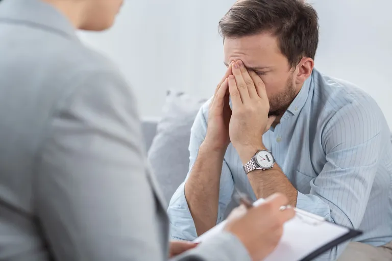 Sad young businessman with problems during session with counselor