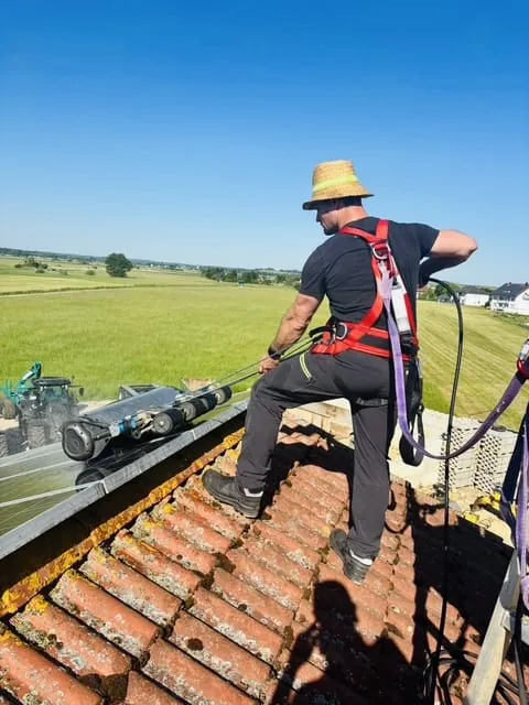 Kaminkehrermeister Florian Prem reinigt auf dem Dach eine PV-Anlage.