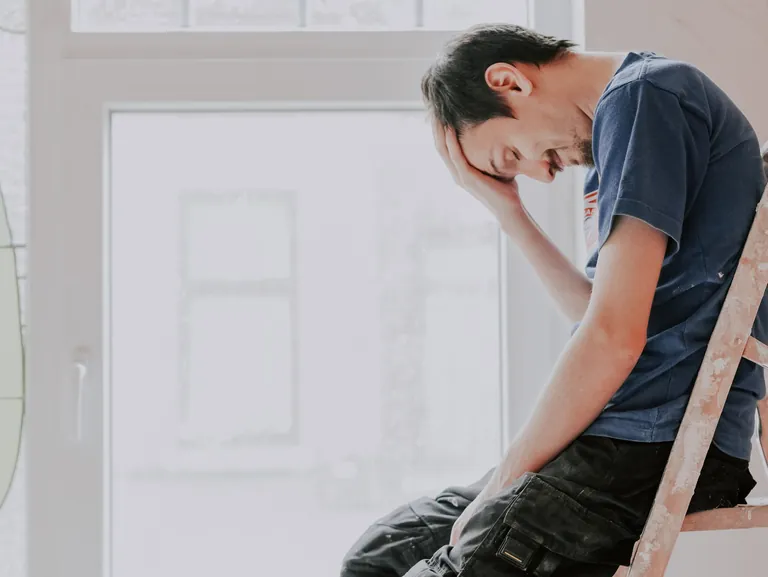 Handwerker mit gesundheitlichen Problemen fasst sich an Kopf