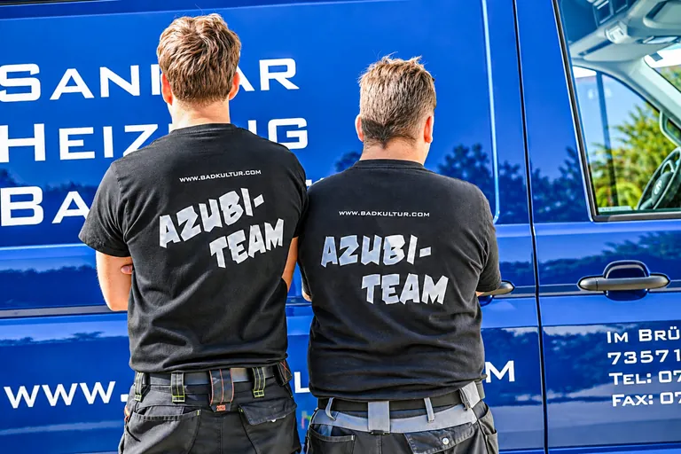 Zwei Auszubildende von hinten, auf deren T-Shirts "Azubi-Team" steht.